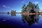 Islands with evergreen trees reflecting in lake, Kejimkujik National Park